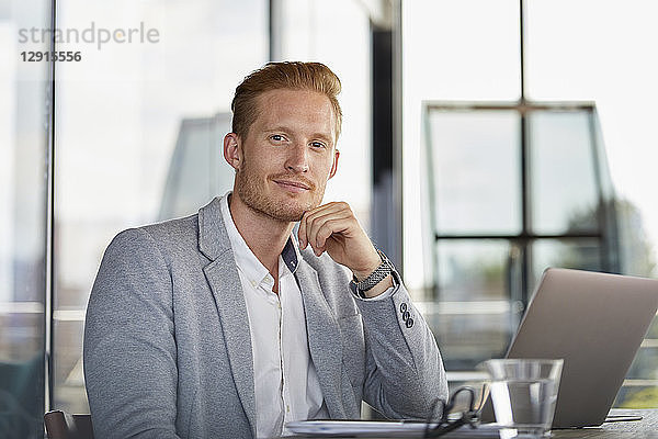 Portrait of confident businessman with laptop on desk in office
