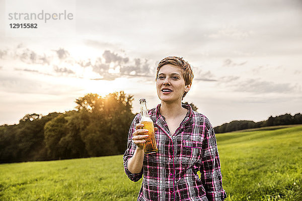 Smiling woman drinking beer in rural landscape