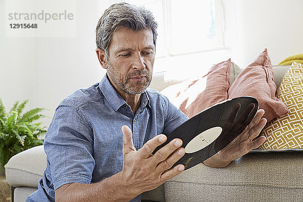 Mature man at home sitting in front of couch  looking at old vinyl record