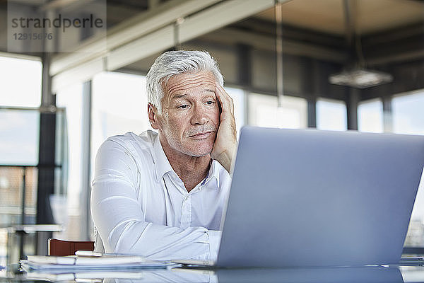 Bored businessman sitting at desk  using laptop