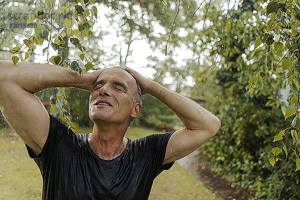 Smiling mature man enjoying summer rain in garden
