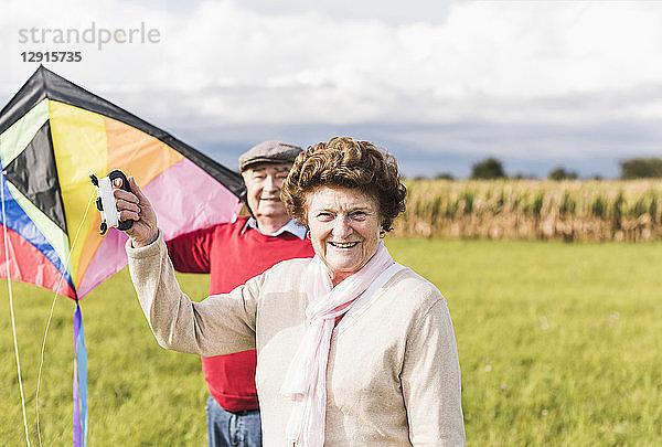 Portrait of smiling senior couple with kite in rural landscape