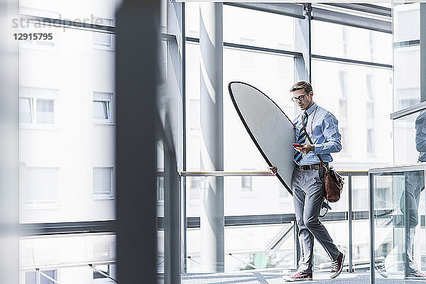 Businessman with cell phone carrying surfboard in office
