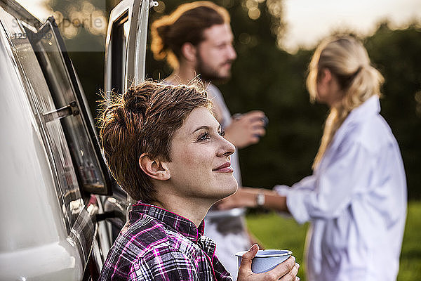 Woman with friends enjoying coffee at a van in rural landscape