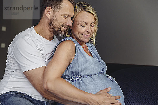 Mature man and his pregnant mature wife sitting on bed touching her belly