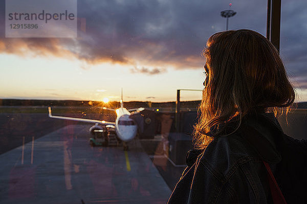 Young woman looking through window on plane at the airport at sunset