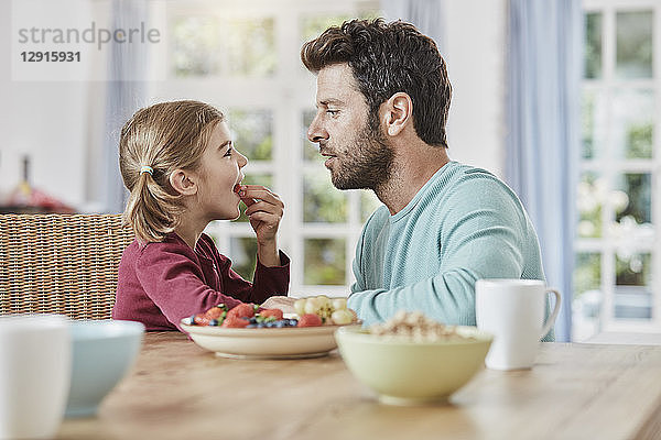 Father and daughter eating fruit at home