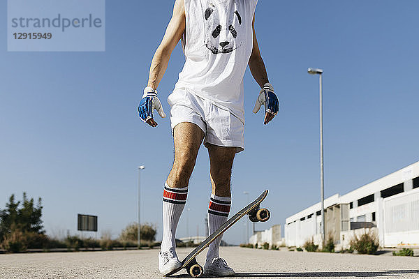 Man in stylish sportive outfit standing on skateboard upside down against blue sky