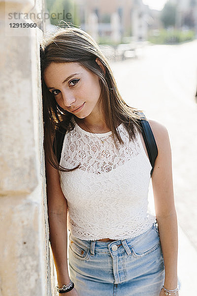 Portrait of smiling young woman leaning against a wall in the city