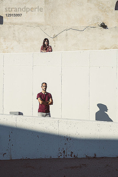 Man and woman standing on different levels of a wall  with arms crossed
