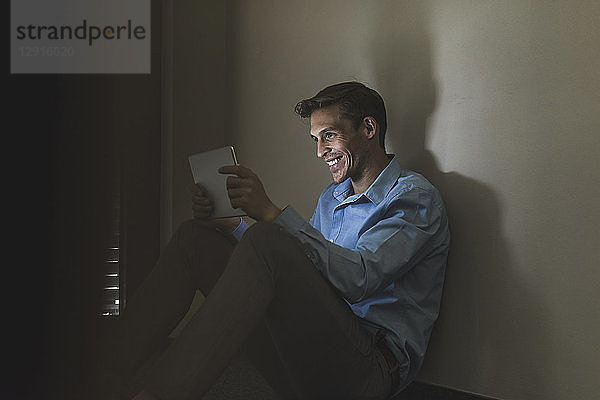 Smiling businessman sitting on the floor using tablet