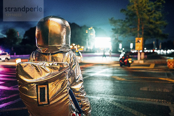 Rear view of spaceman on a street in the city at night attracted by shining projection screen