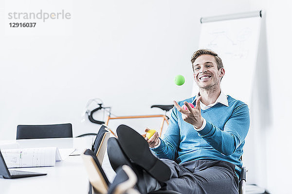 Smiling businessman juggling with balls in office