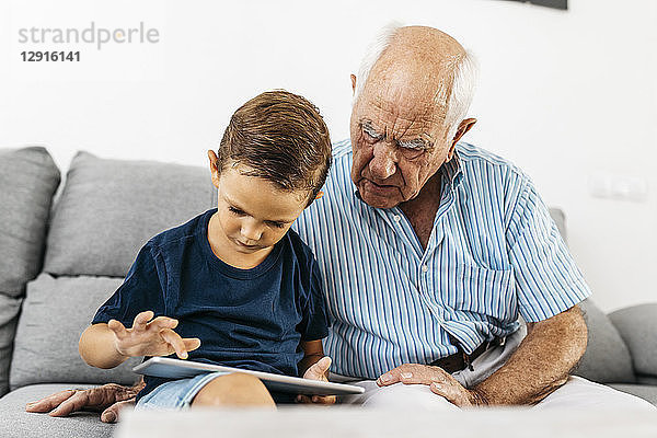 Grandfather and grandson sitting together on the couch at home using digital tablet