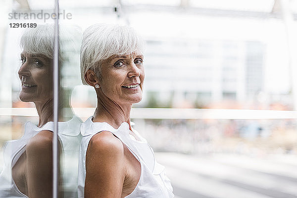 Portrait of smiling senior woman leaning against glass facade