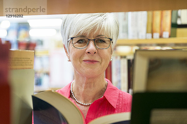 Portrait of smiling senior woman with book in a city library