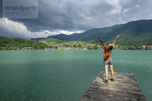 Teenager standing on wooden jetty  raised arms