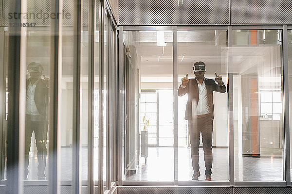 Businessman standing in office building  looking through VR goggles