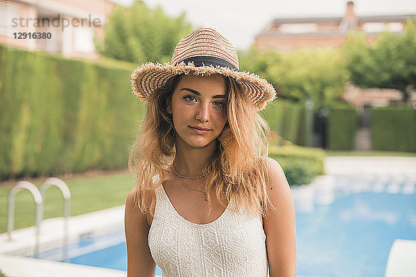 Portrait of young woman with straw hat and swimsuit  pool in the background