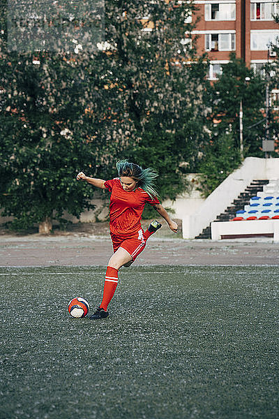 Young woman playing football on football ground shooting the ball