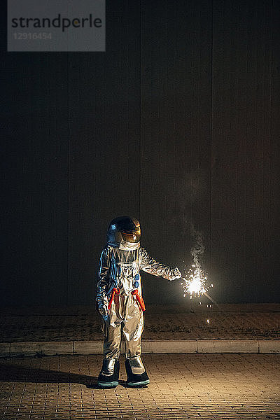 Spaceman standing on a road at night holding sparkler