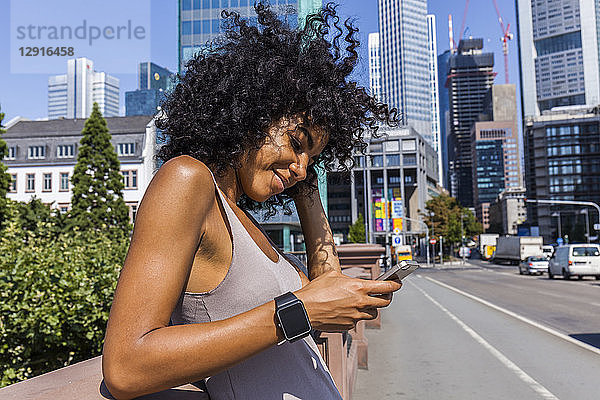 Germany  Frankfurt  portrait of smiling young woman with curly hair using cell phone in the city