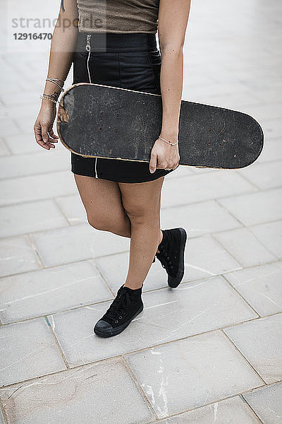 Low section of young woman carrying skateboard