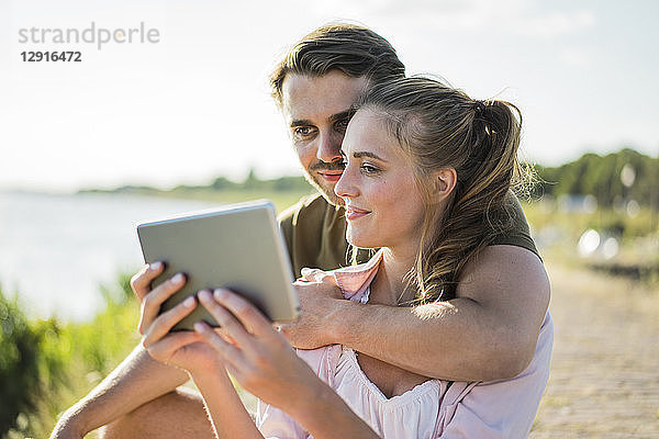 Smiling couple at the riverside in summer holding tablet