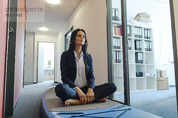 Businesswoman practicing yoga on paddle board  daydreaming in office