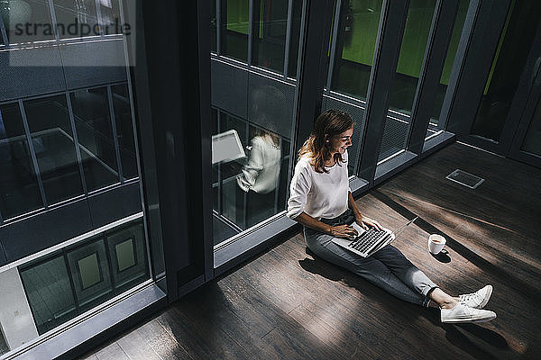 Businesswoman sitting on ground in empty office  using laptop