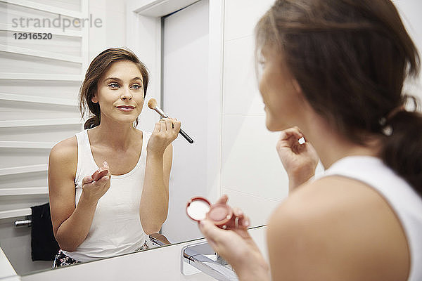 Mirror image of smiling young woman applying Makeup in bathroom