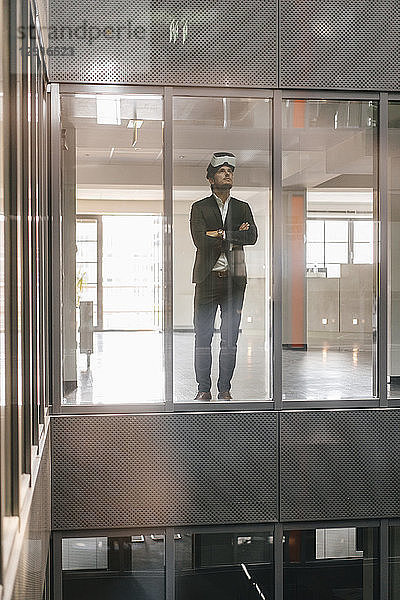 Businessman standing in office building  looking through VR goggles