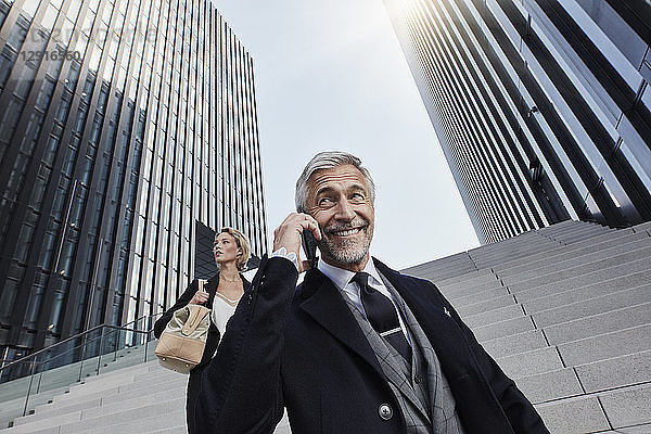 Portrait of smiling businessman on the phone with his business partner in the background