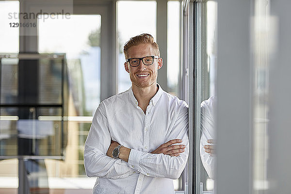 Portrait of smiling businessman in office leaning against window