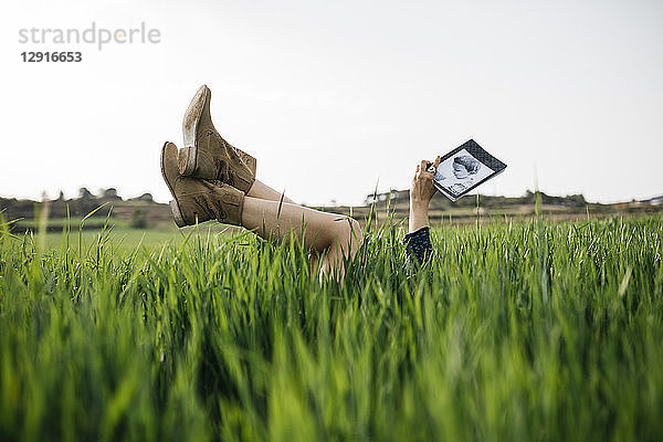Woman lying on a field with legs in the air reading a book