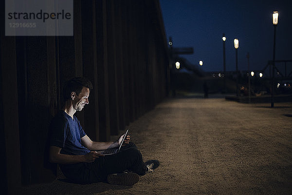 Mid adult man sitting cross-legged on ground  using laptop at night