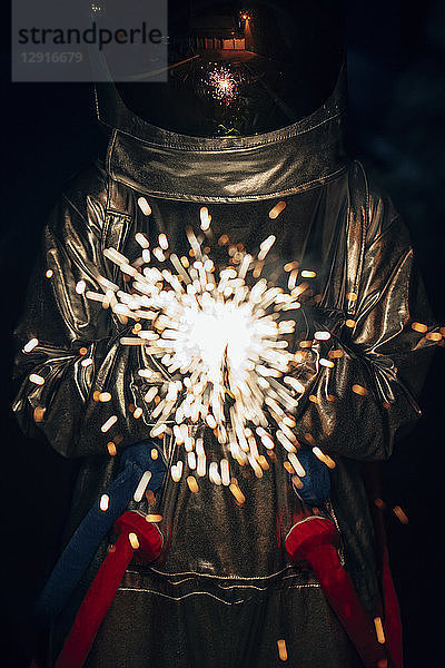Spaceman standing outdoors at night holding sparkler