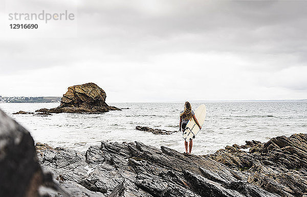 Young woman carrying surfboard on a rocky beach at the sea