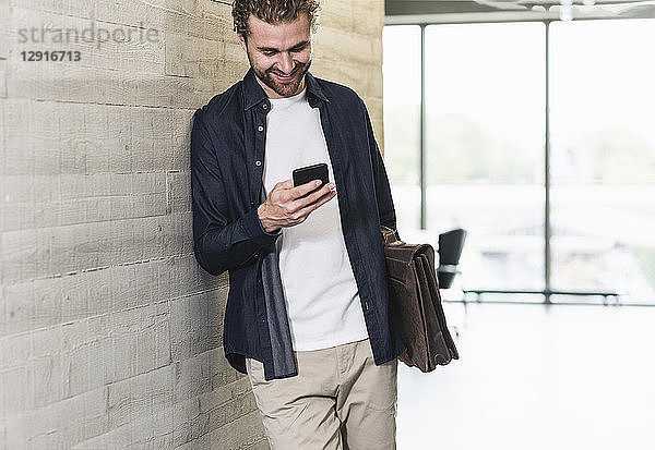 Smiling casual businessman standing on office floor checking cell phone