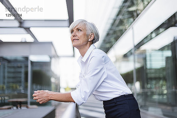 Senior woman leaning on railing in the city looking up