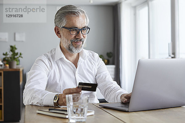Portrait of content mature man paying online with credit card at home