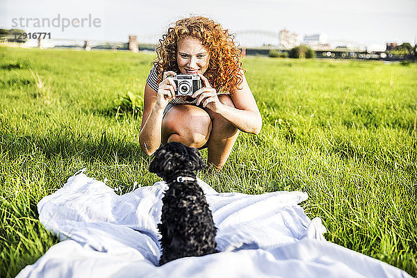 Germany  Cologne  portrait of smiling young woman on meadow taking picture of her dog