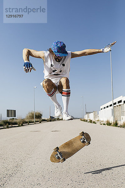 Sportive man jumping above ground with skateboard performing trick