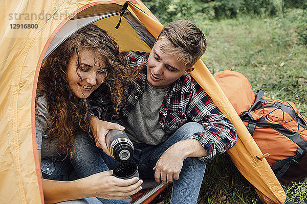 Young couple sitting in tent  drinking tea