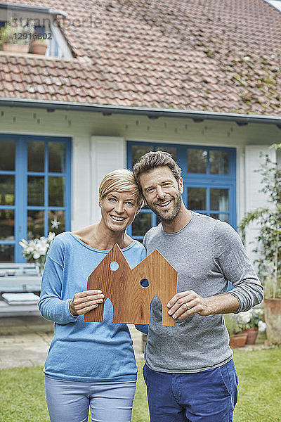 Portrait of smiling couple standing in front of their home holding house model