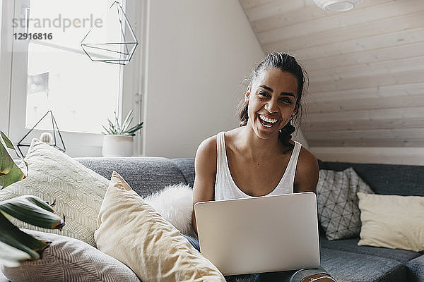 Portrait of laughing woman sitting with laptop on the couch at home