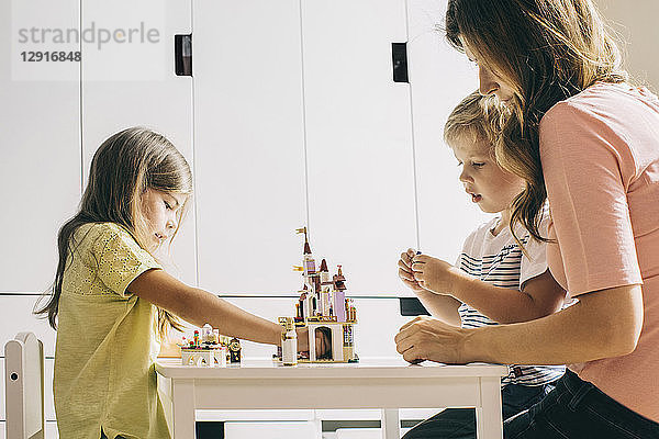 Mother with two children building up toy castle at home