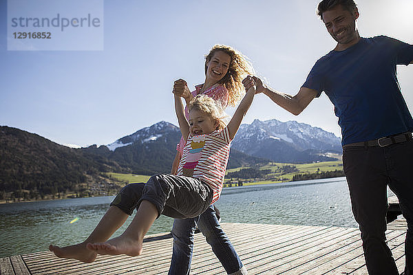 Austria  Tyrol  Walchsee  happy parents swinging their daughter at the lake