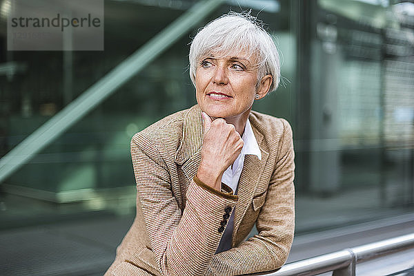 Portrait of senior businesswoman leaning on railing in the city looking around