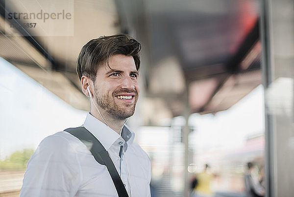 Portrait of smiling businessman on station platform with earphones